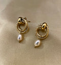 Close-up detail of textured gold hoop earrings featuring a dainty oval pearl drop. The earrings are worn on the ear to show scale, highlighting the metallic luster and elegant Parisian chic design against a neutral background.