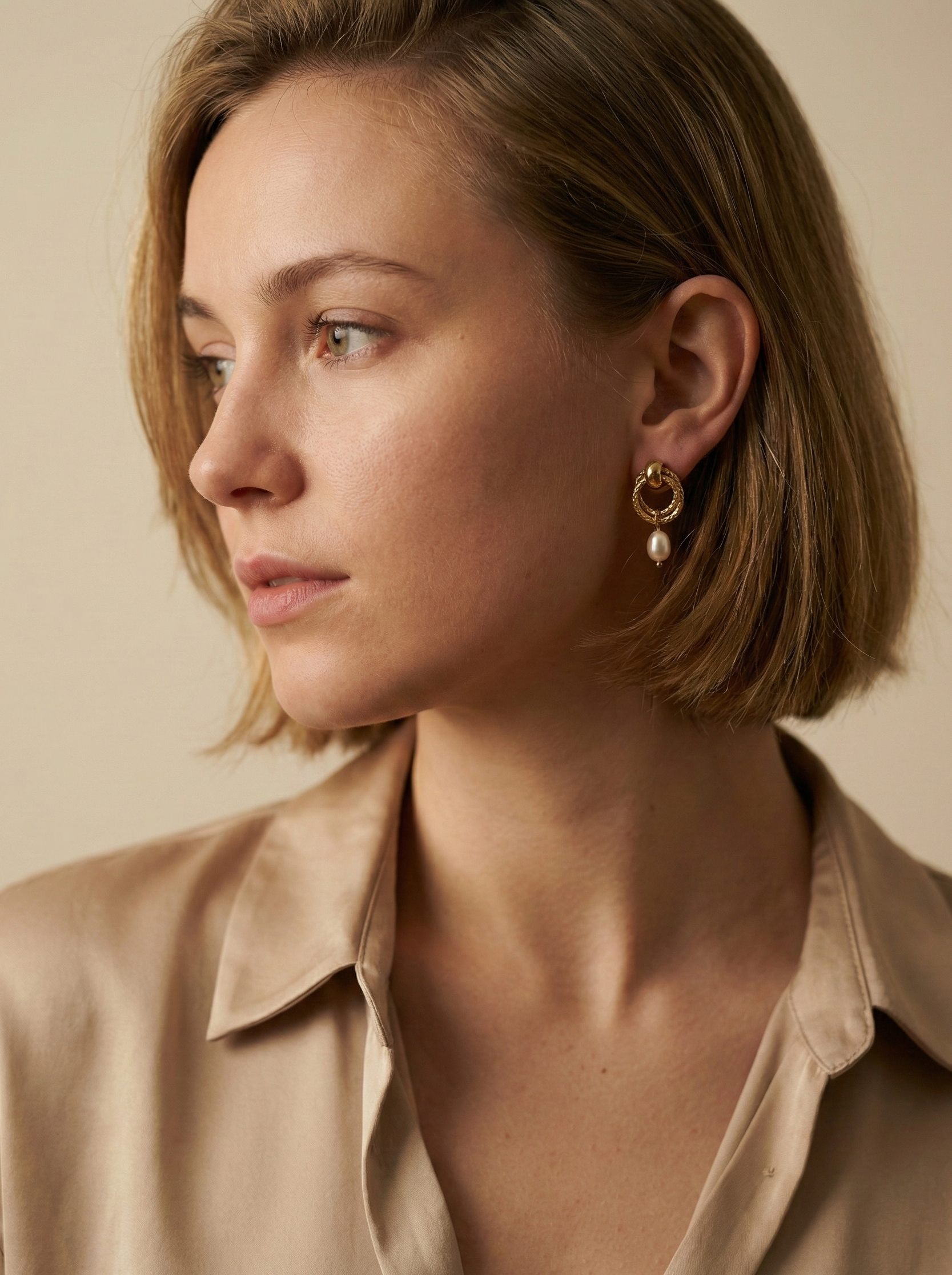 Women's textured gold interlocking hoop earrings with a genuine white pearl charm. High-resolution jewelry detail shot showing the clasp and finish.