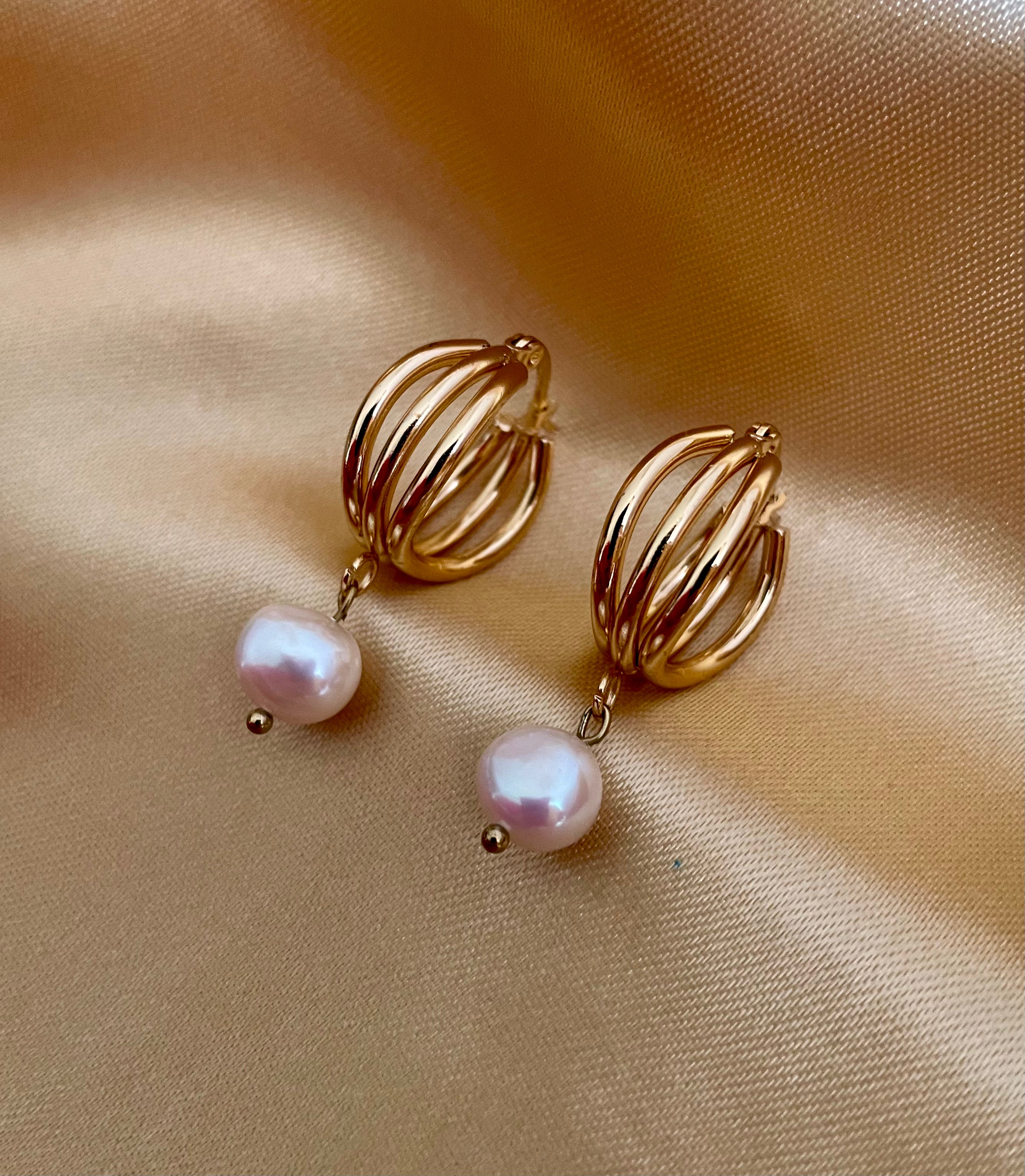 Luxury gold huggie earrings with white baroque pearl drop on model ear. High-luster freshwater pearl jewelry with triple-split gold hoop design in an editorial close-u