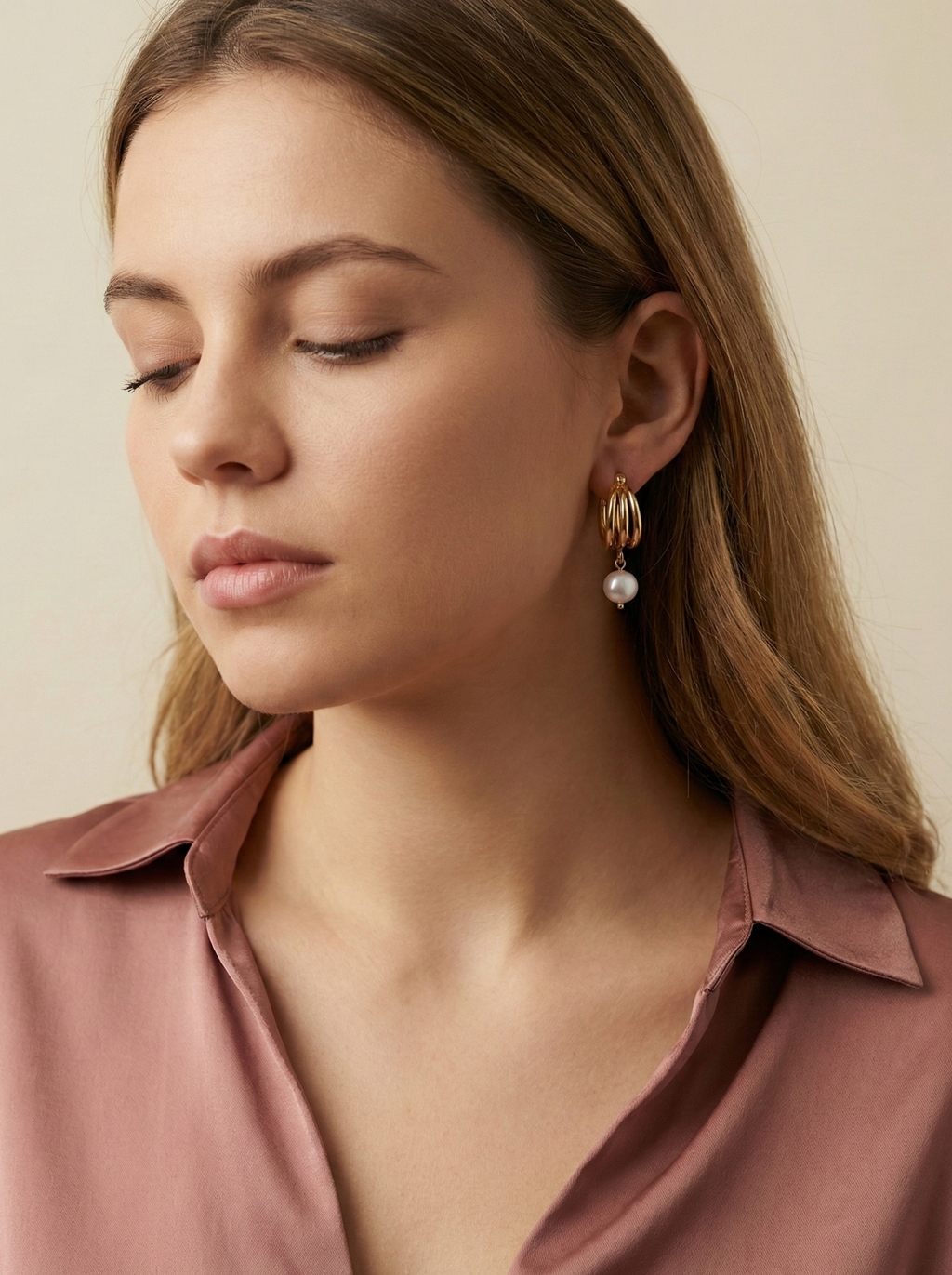 Luxury gold huggie earrings with white baroque pearl drop on model ear. High-luster freshwater pearl jewelry with triple-split gold hoop design in an editorial close-up