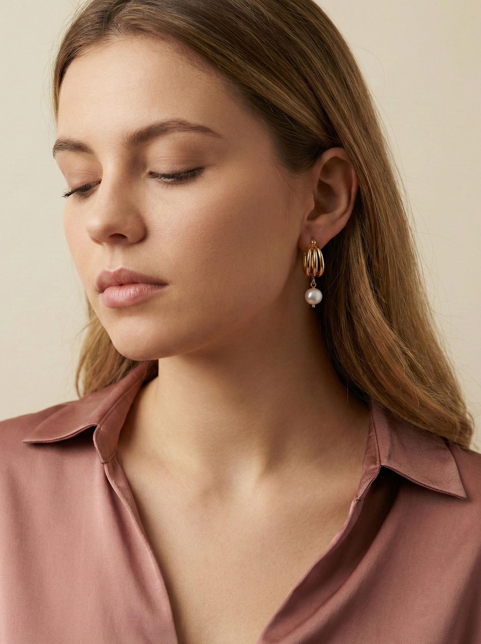 Luxury gold huggie earrings with white baroque pearl drop on model ear. High-luster freshwater pearl jewelry with triple-split gold hoop design in an editorial close-up