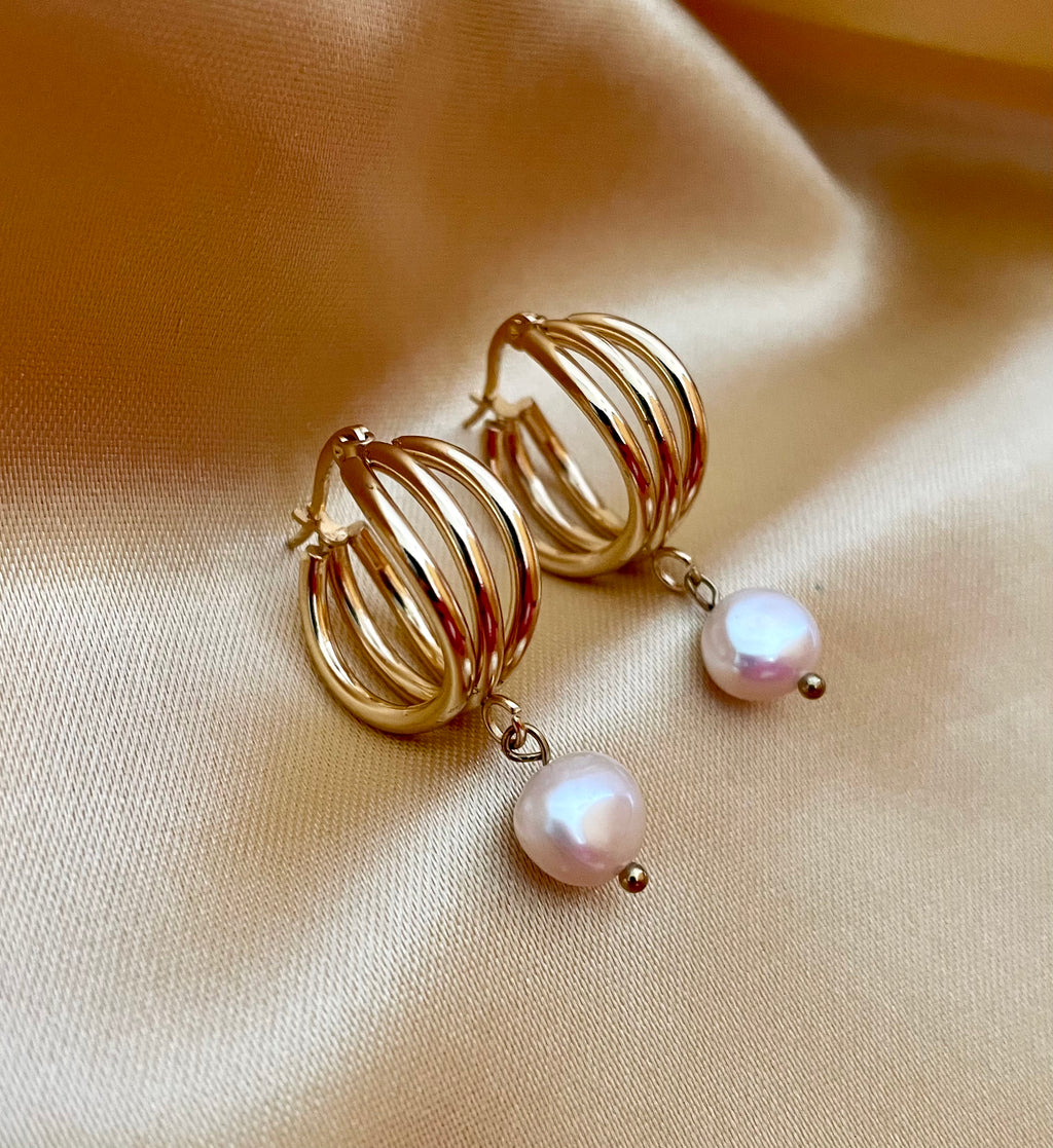 Luxury gold huggie earrings with white baroque pearl drop on model ear. High-luster freshwater pearl jewelry with triple-split gold hoop design in an editorial close-u