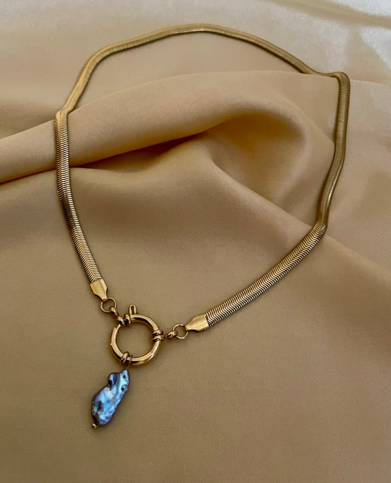 flat gold herringbone chain necklace featuring a front toggle clasp and an elongated grey keshi pearl pendant, styled with a deep V-neck ivory silk top