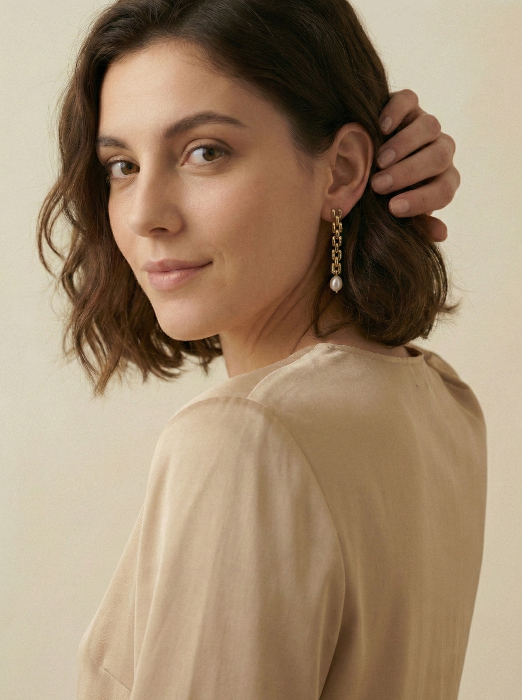 Gold rectangular link chain drop earrings featuring luminous white oval pearls on a beige silk background. Handcrafted Parisian pearl jewelry