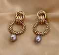 Close-up detail of textured gold interlocking hoop earrings featuring a lustrous metallic grey pearl drop. The design includes a beaded gold circle and polished gold links
