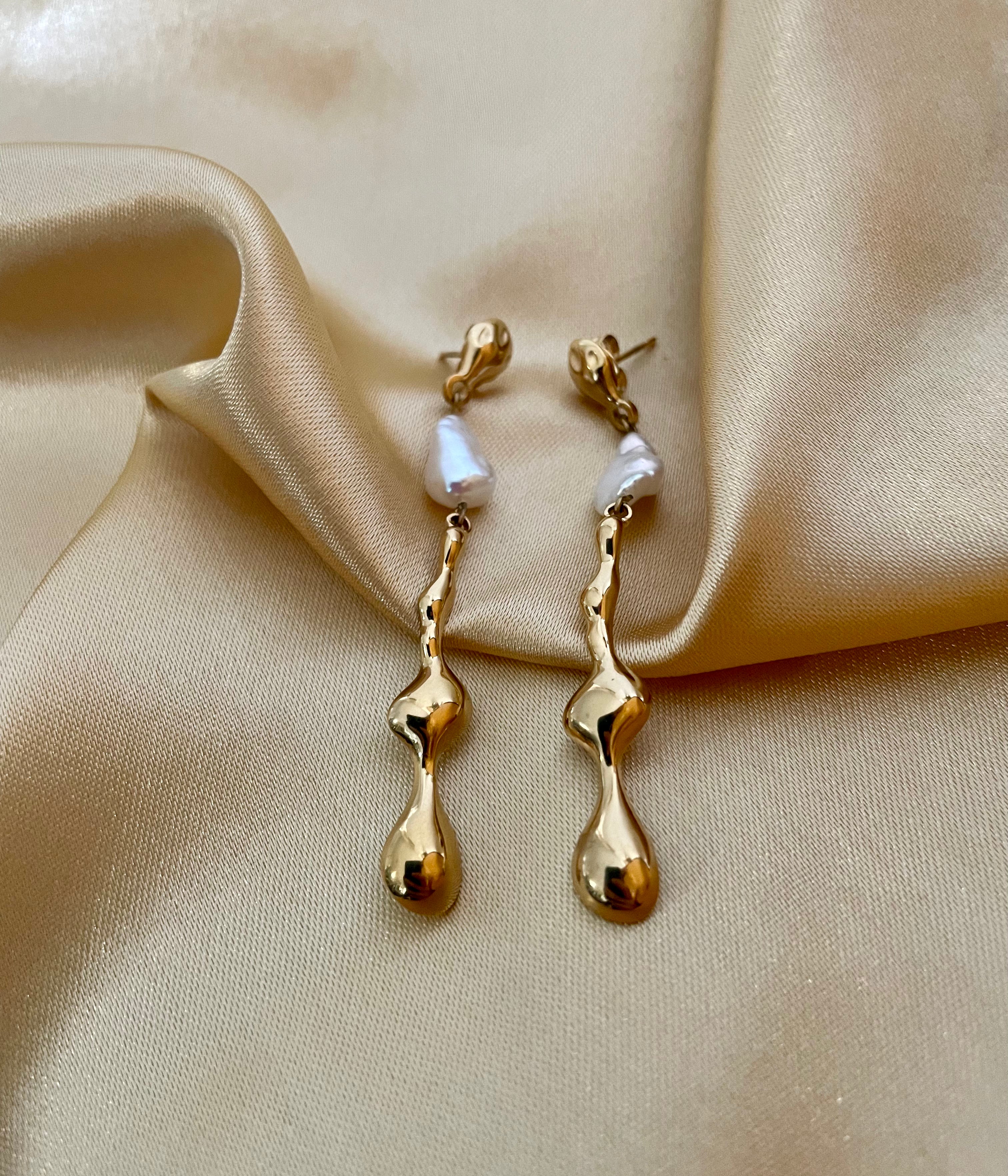 Gold earrings with pearls on a beige fabric background