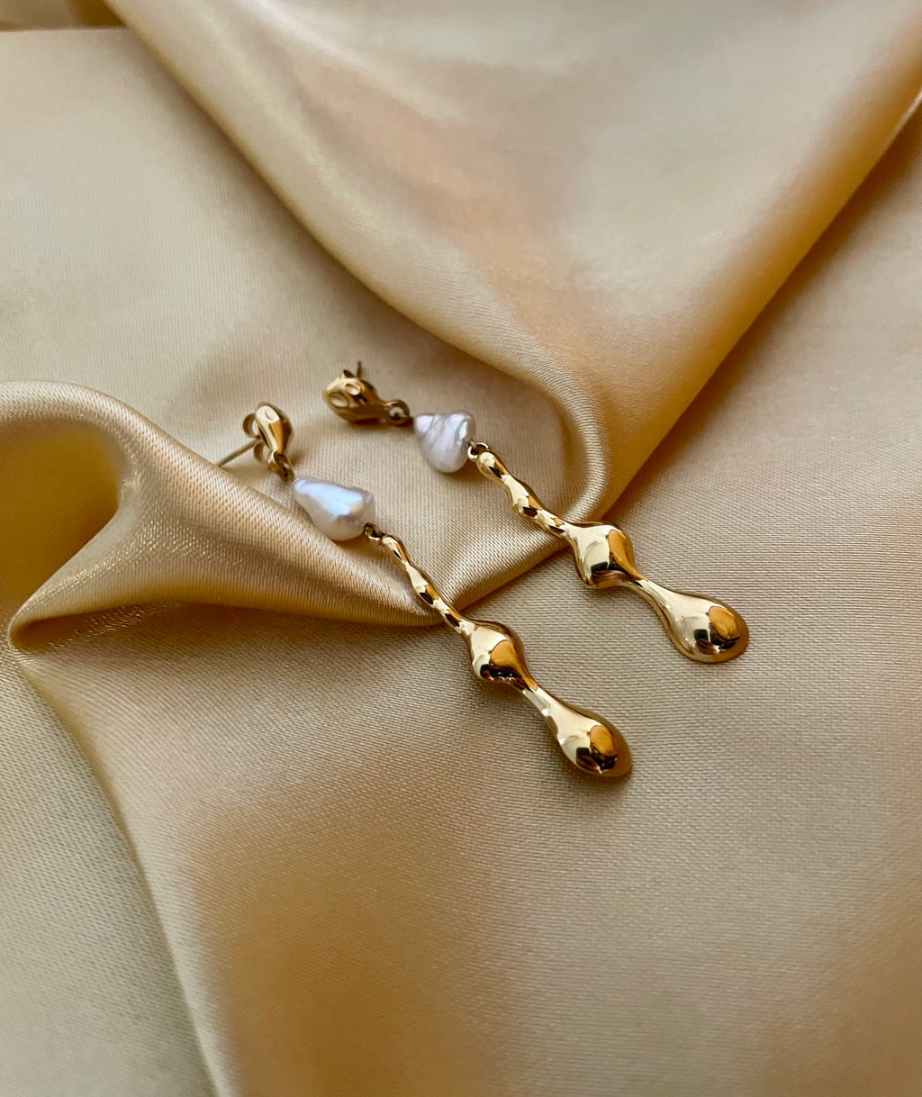 Gold earrings with keshi pearls on beige fabric