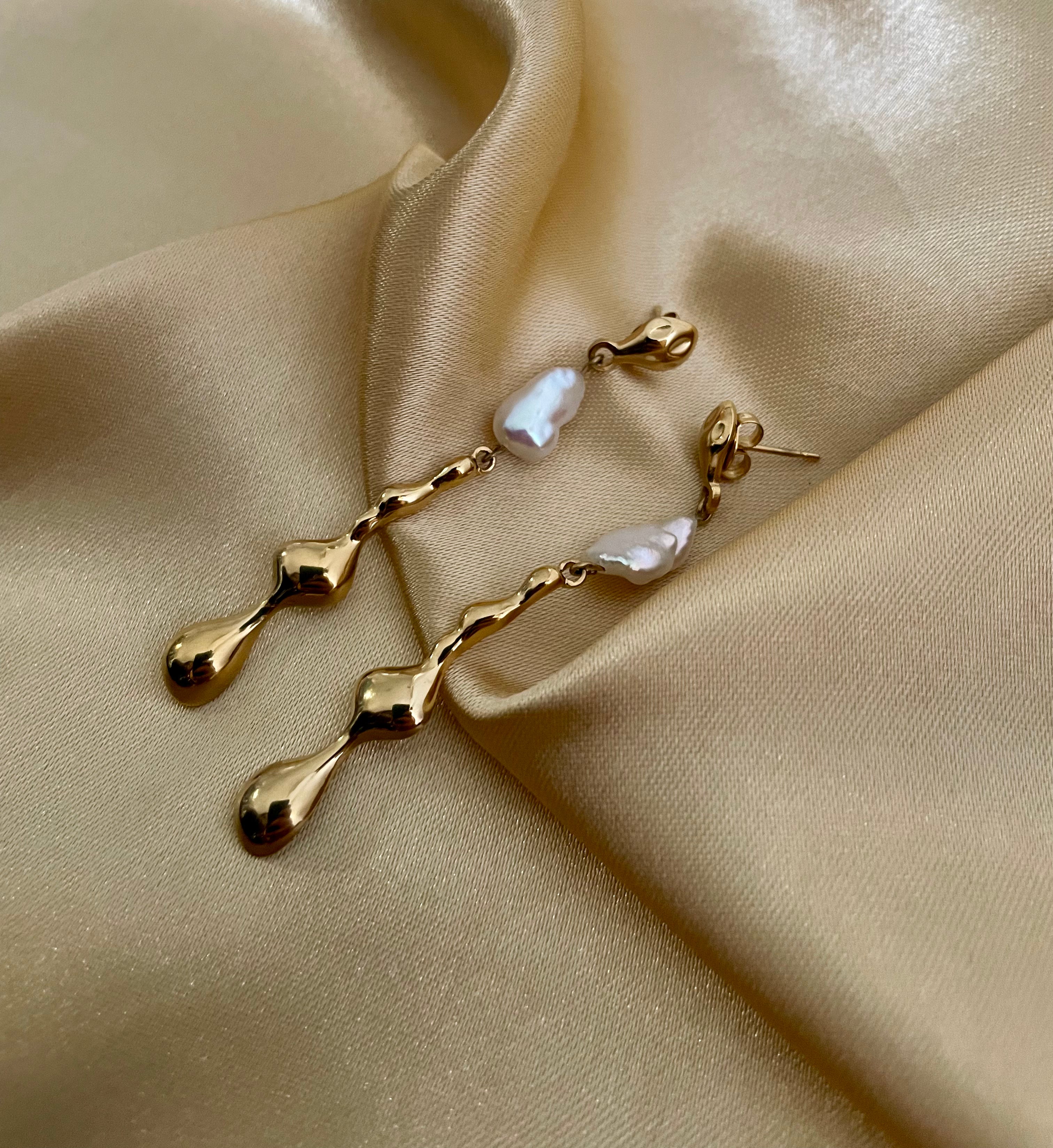 Gold earrings with pearls on a beige satin background