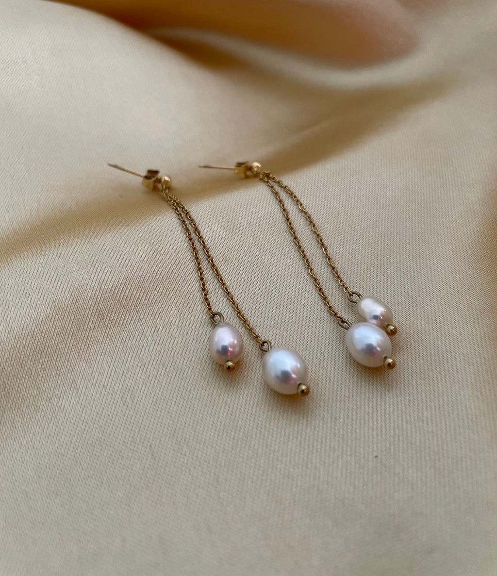 white and champagne pearl earrings with gold chains on a beige fabric background