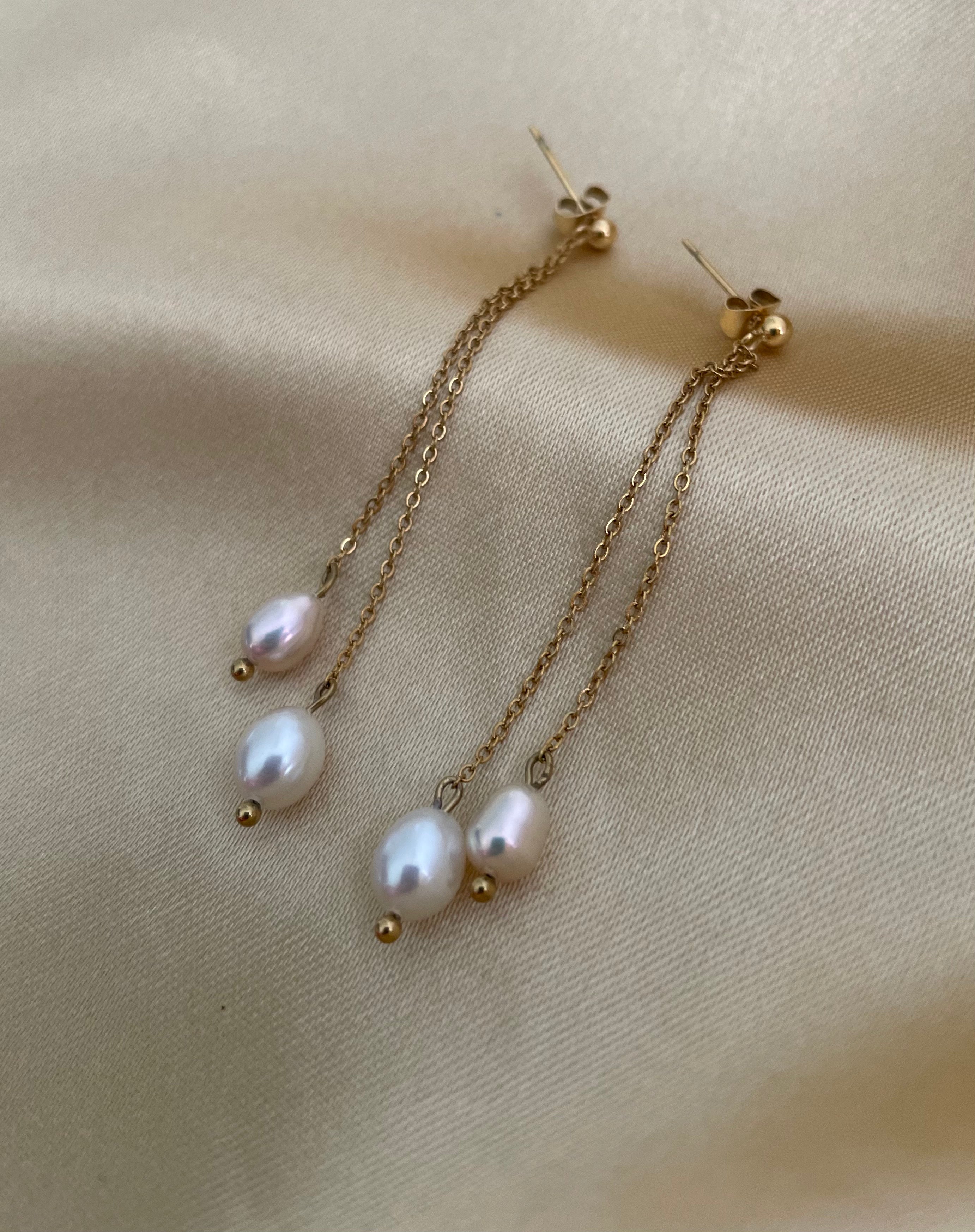 white and champagne pearl earrings with gold chains on a beige fabric background
