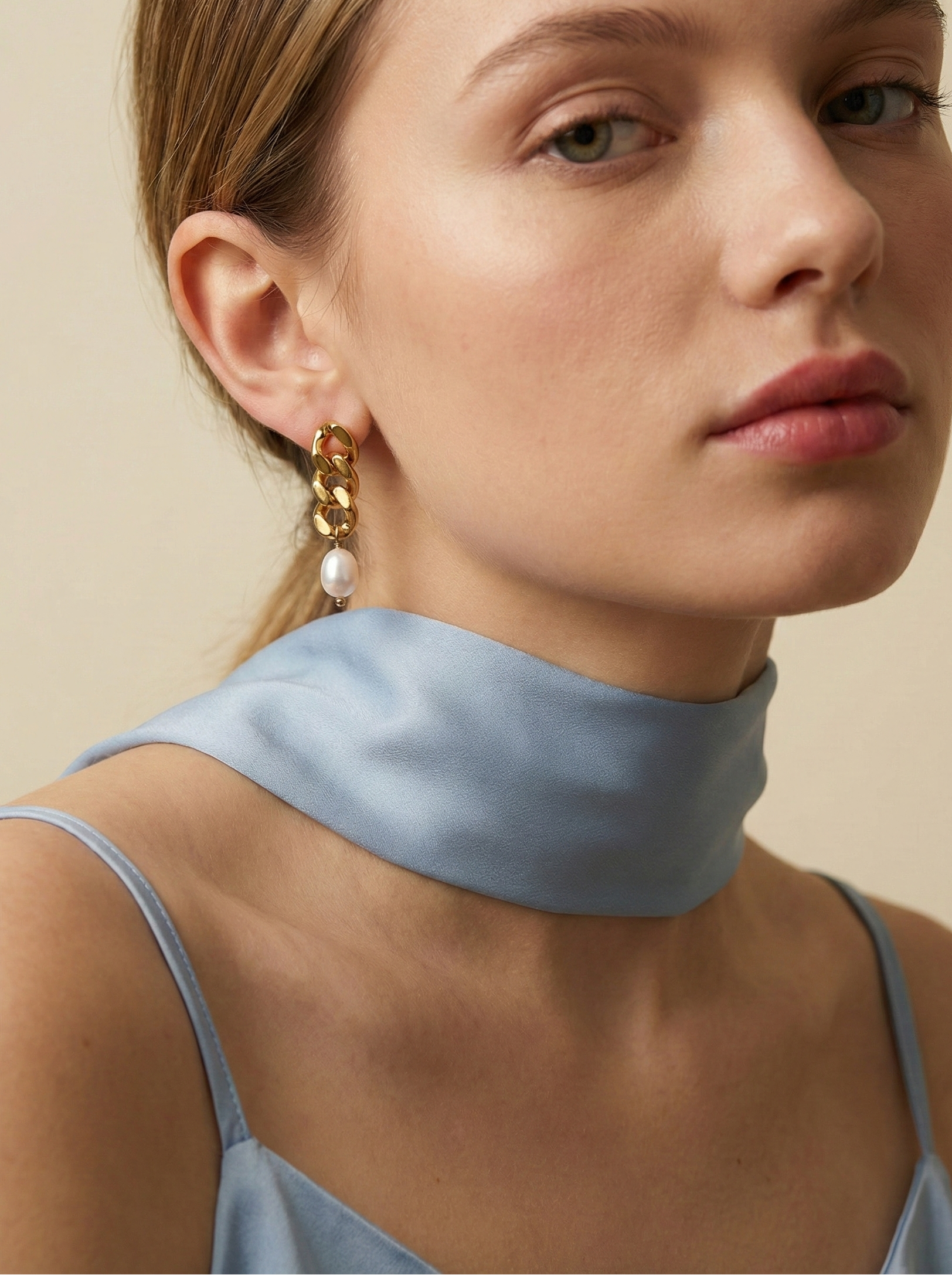 Close-up of gold chain link earrings featuring a lustrous oval white pearl drop. The earrings are shown on a model to demonstrate scale, featuring a high-polish gold finish and organic pearl shape
