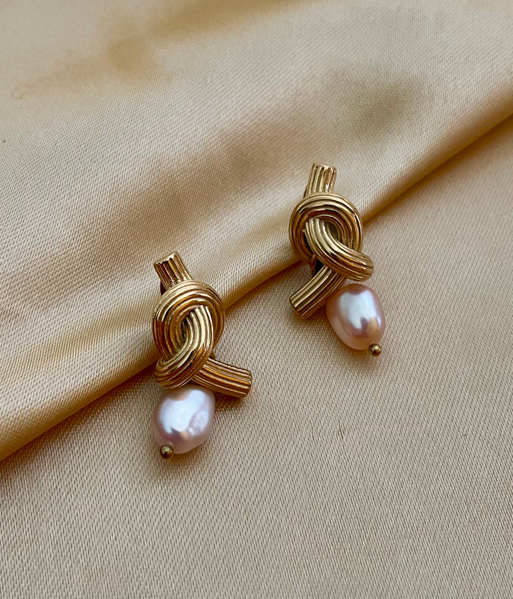 Close-up editorial photography of ribbed gold twisted knot earrings featuring a lustrous pink oval pearl drop