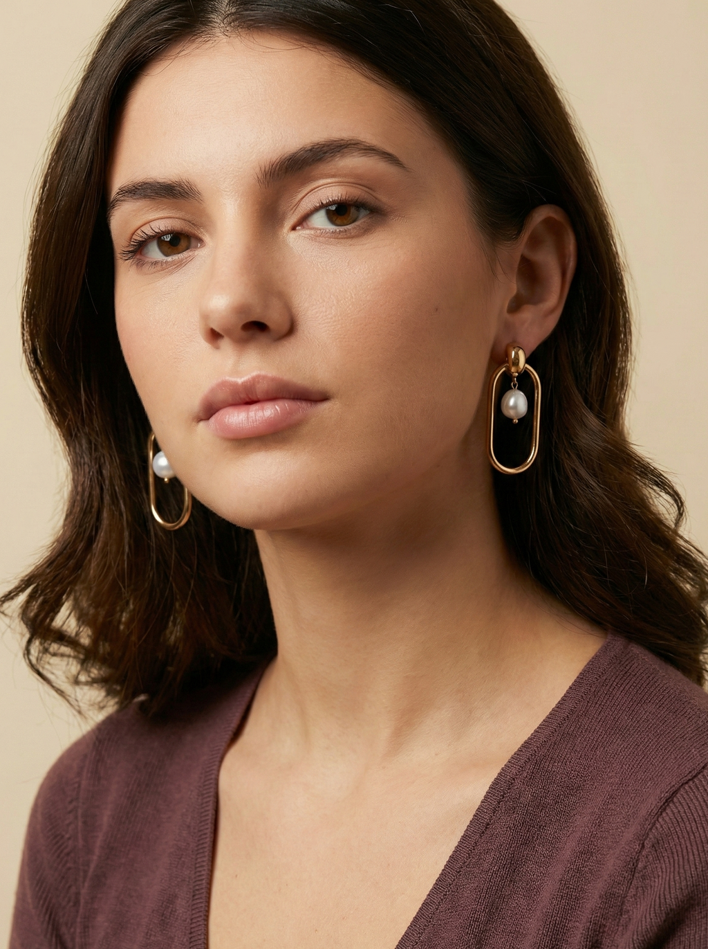 Editorial shot of a model wearing modern geometric gold hoop earrings with a floating freshwater pearl center, set against a warm ivory background