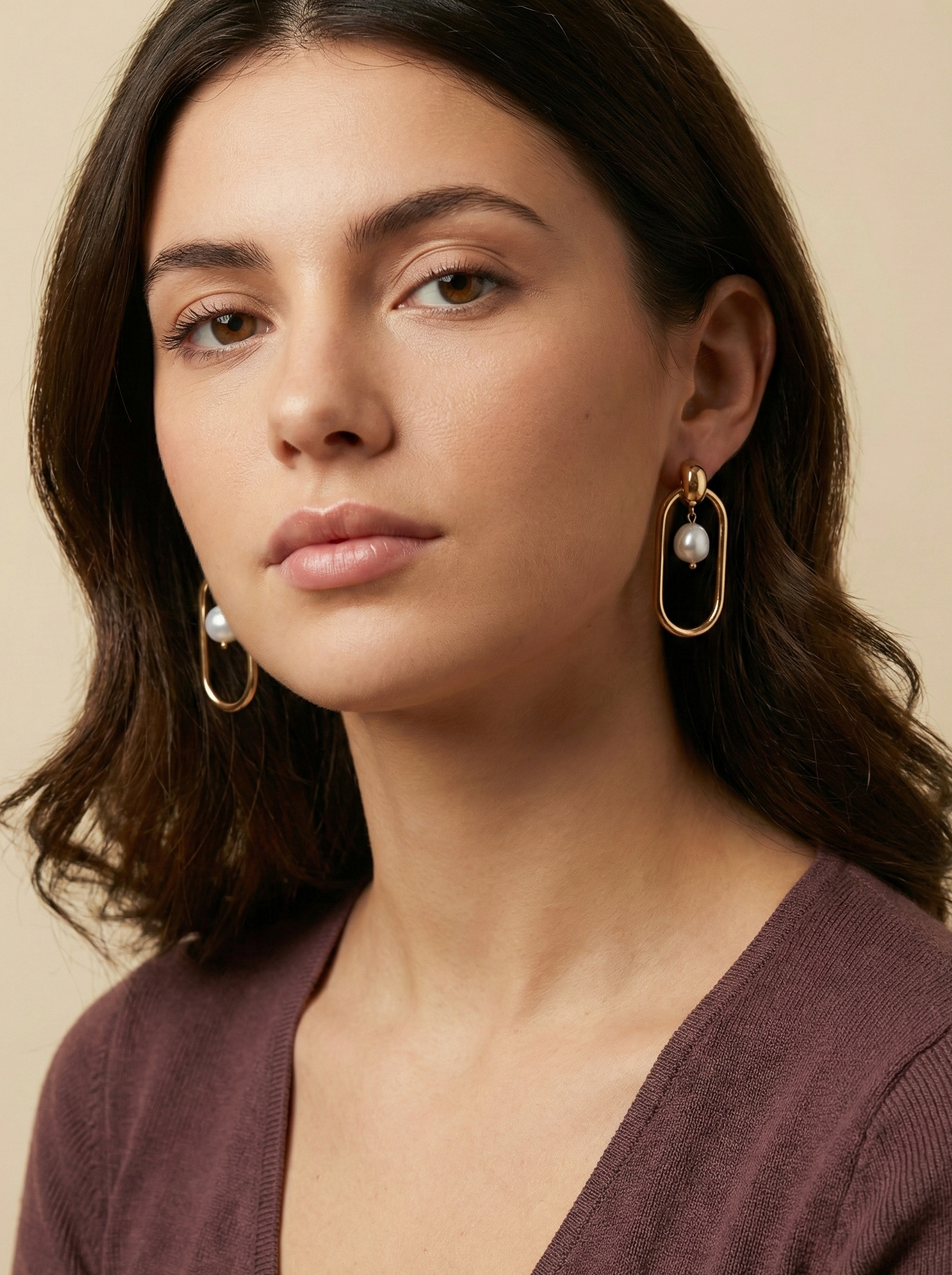 Editorial shot of a model wearing modern geometric gold hoop earrings with a floating freshwater pearl center, set against a warm ivory background
