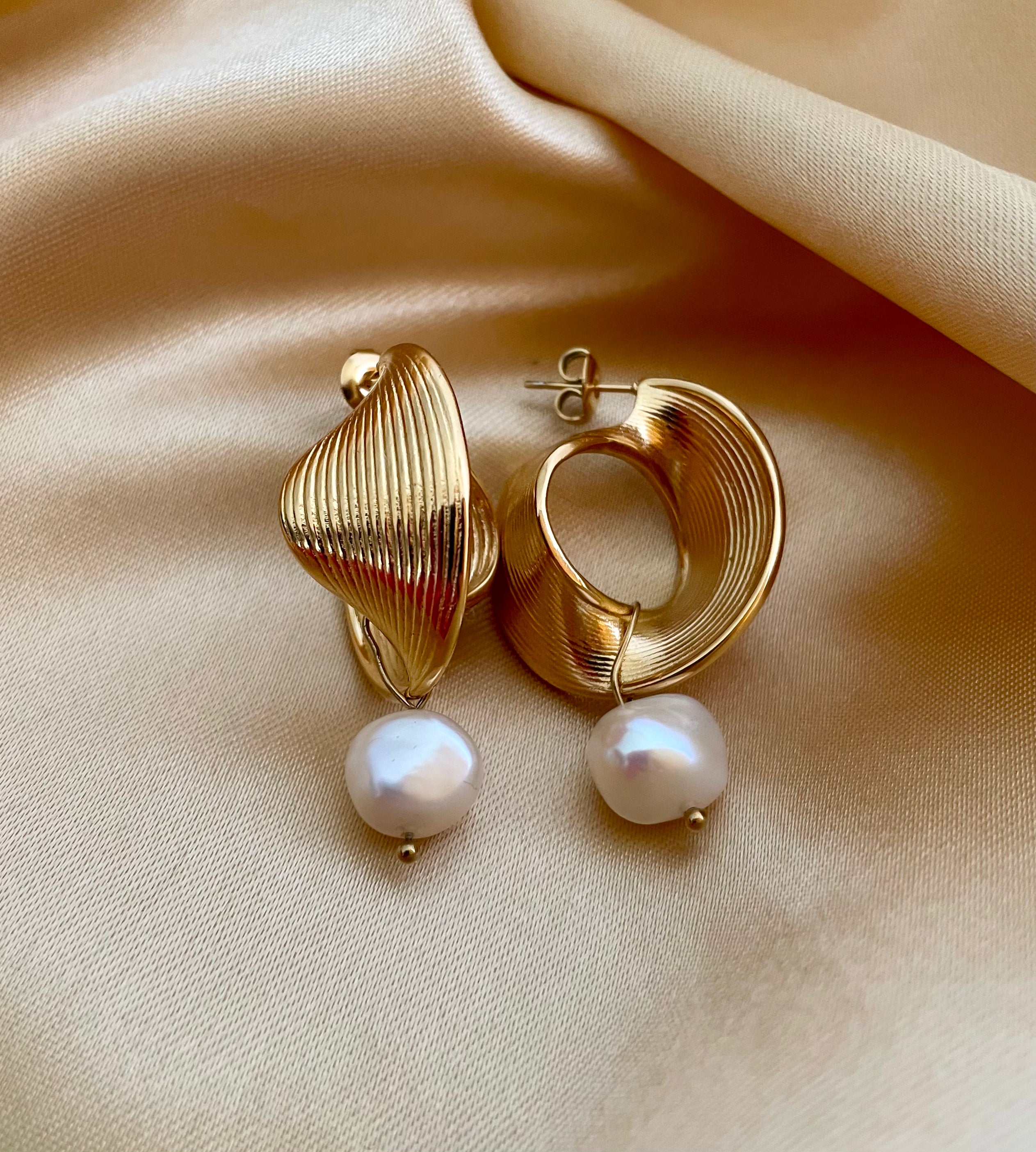 Editorial portrait of a woman wearing a white silk top styled with modern architectural gold earrings and lustrous pearl charms.