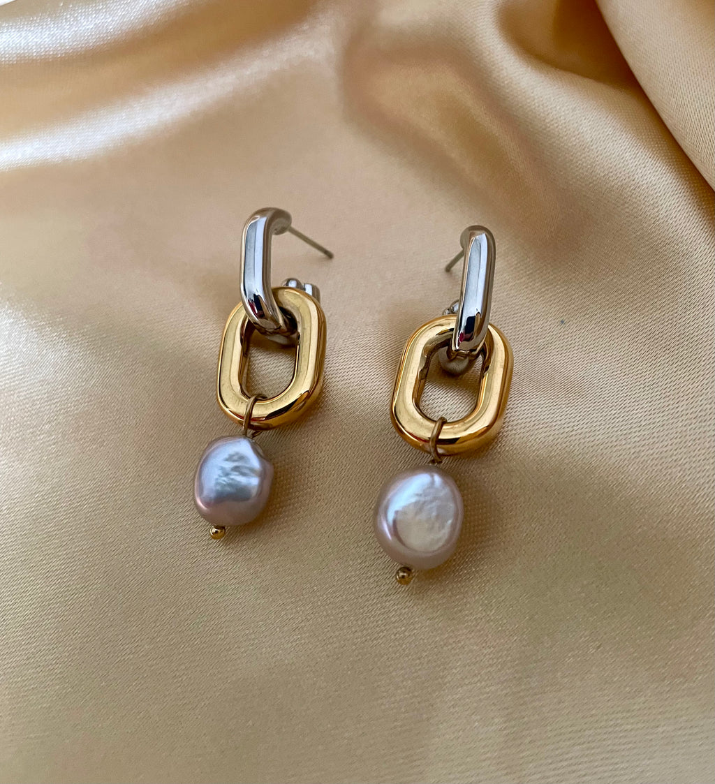 Close-up detail of mixed metal chain link earrings with grey pearl drops worn on the ear.