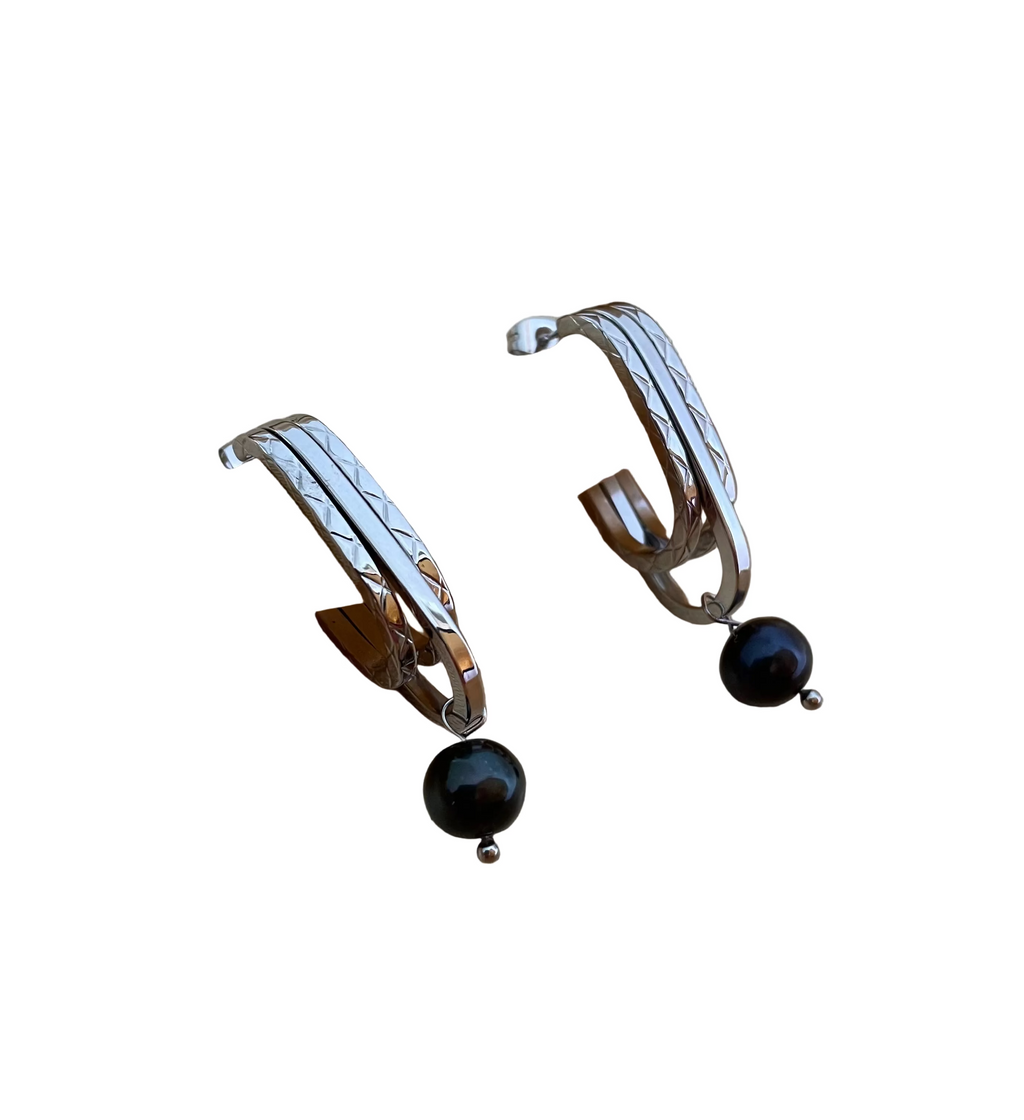 Close-up detail of AAA quality round black freshwater pearl on PVD 18k gold plated stainless steel drop earrings. High-lustre dark pearl texture.