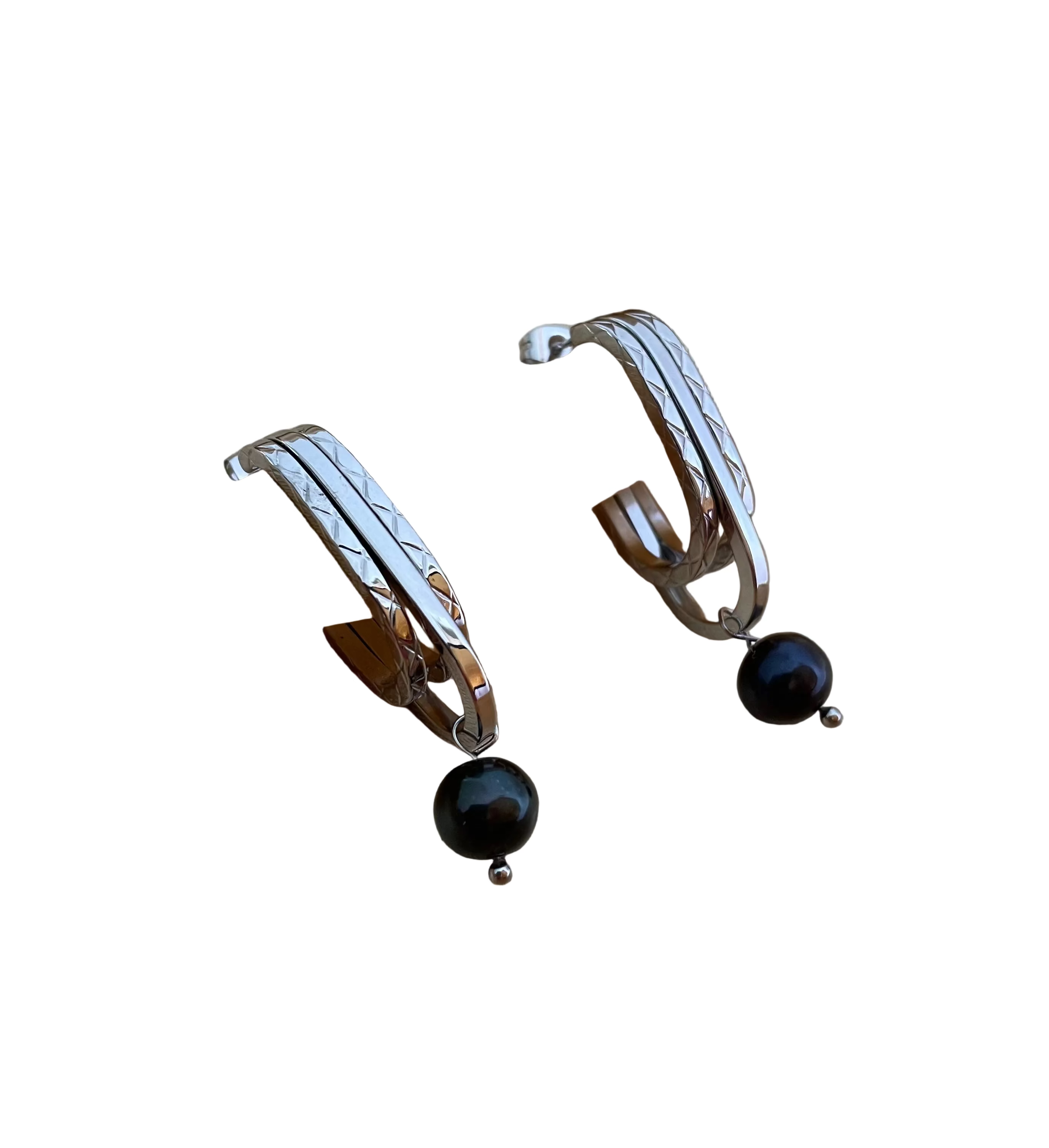 Close-up detail of AAA quality round black freshwater pearl on PVD 18k gold plated stainless steel drop earrings. High-lustre dark pearl texture.