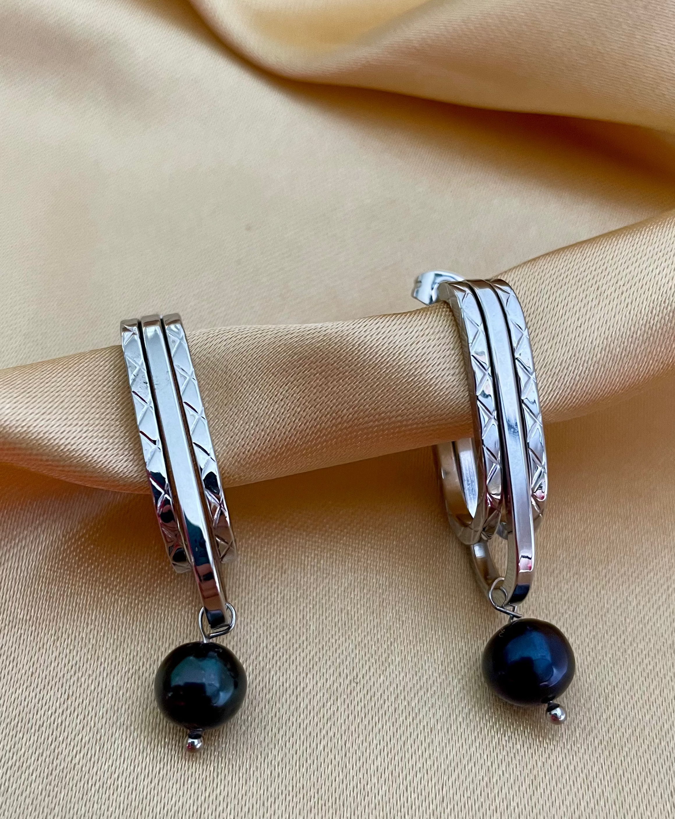 Close-up detail of AAA quality round black freshwater pearl on PVD 18k gold plated stainless steel drop earrings. High-lustre dark pearl texture.