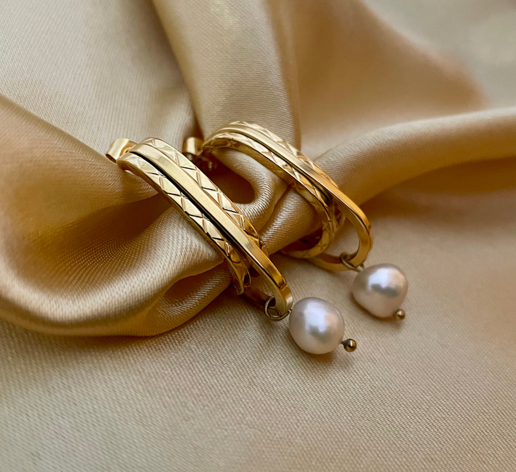 Close-up detail of AAA quality round white freshwater pearl on PVD 18k gold plated stainless steel drop earrings. High-lustre pearl texture.
