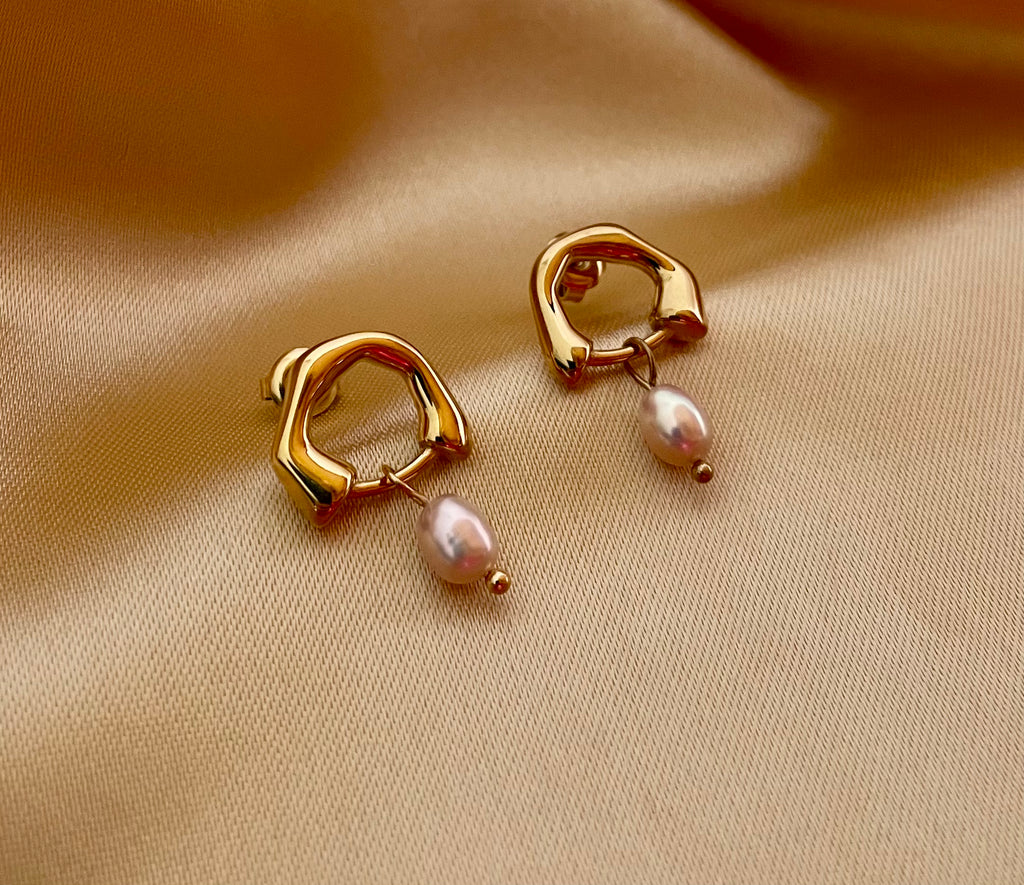 Close-up detail of organic gold huggie hoop earrings featuring a high-luster pink oval freshwater pearl drop