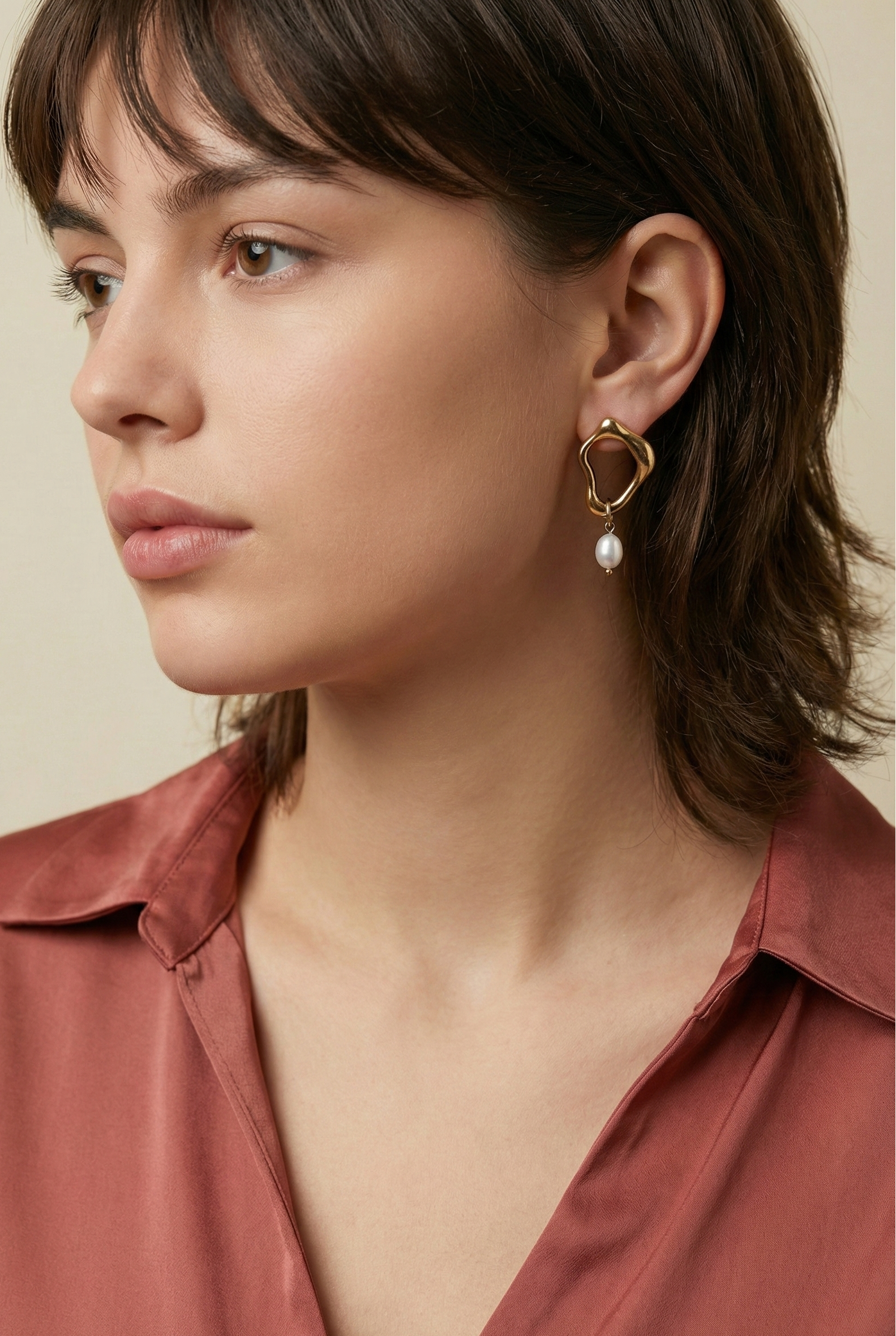 Close-up detail of organic-shaped gold drop earrings featuring a small freshwater white oval pearl, worn by a model with a side profile view