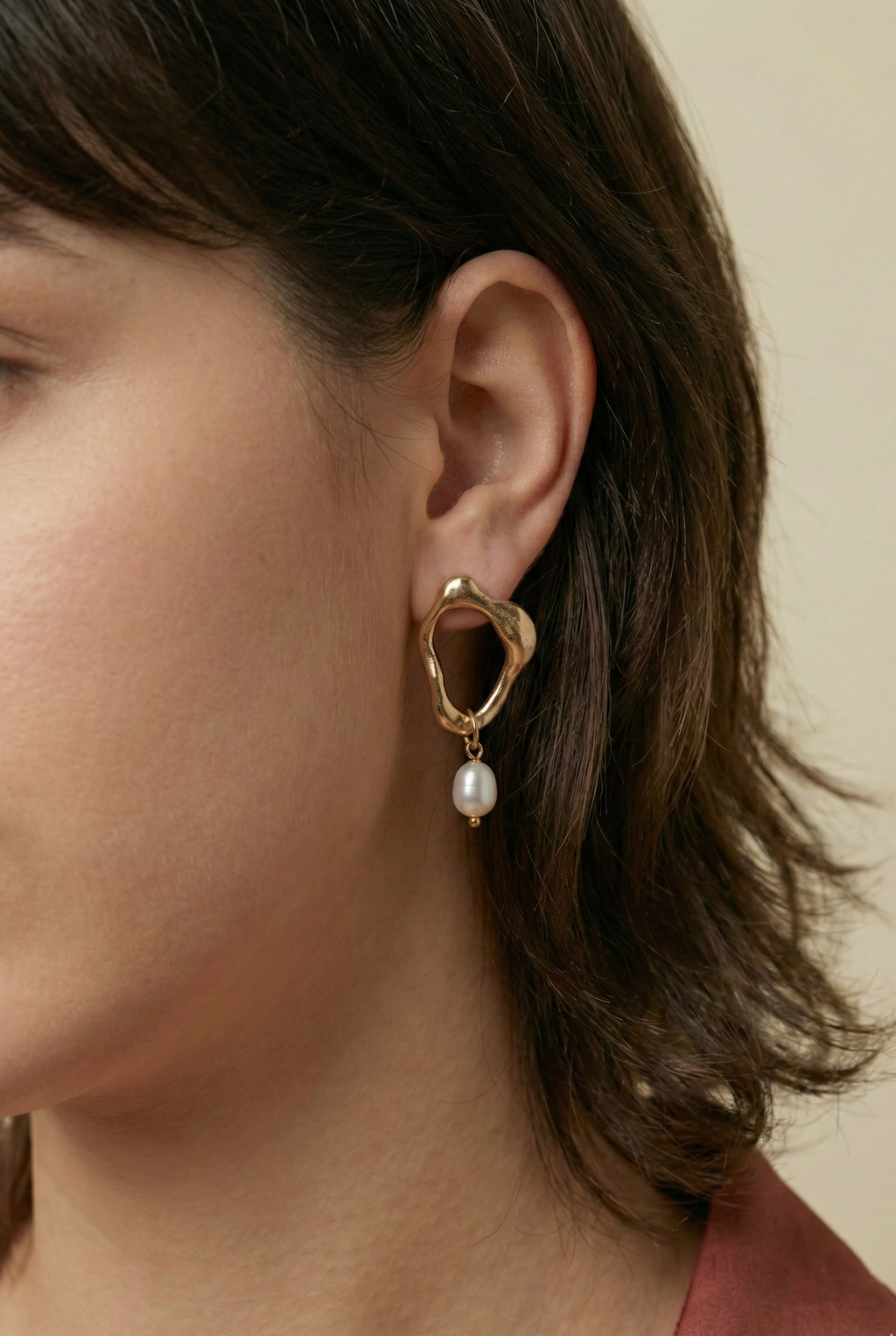 Close-up detail of organic-shaped gold drop earrings featuring a small white oval pearl