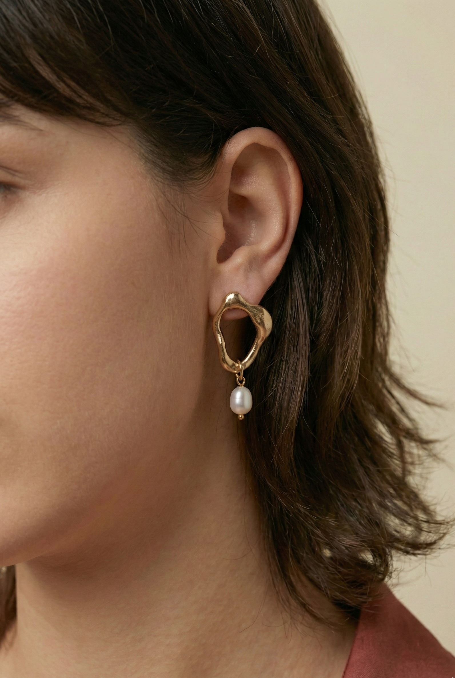 Close-up detail of organic-shaped gold drop earrings featuring a small white oval pearl