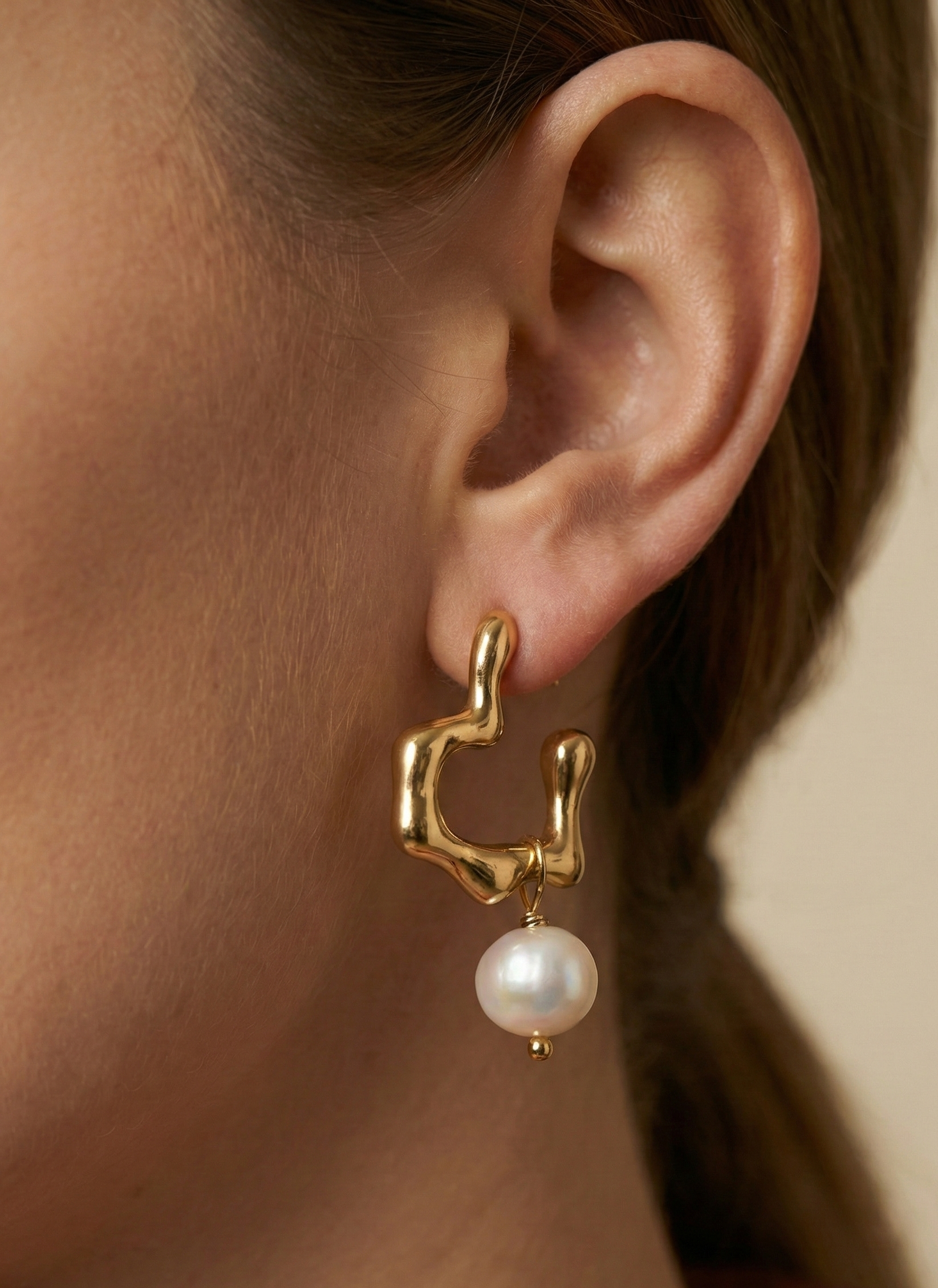 Close-up of model wearing organic sculptural gold hoop earrings with a freshwater pearl drop. Modern 18k gold plated wavy hoops styled for everyday luxury