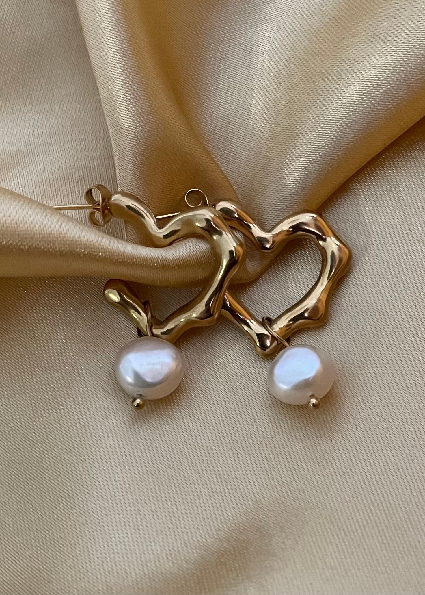 Close-up of an organic sculptural gold hoop earrings with a freshwater pearl drop. Modern 18k gold plated wavy hoops styled for everyday luxury