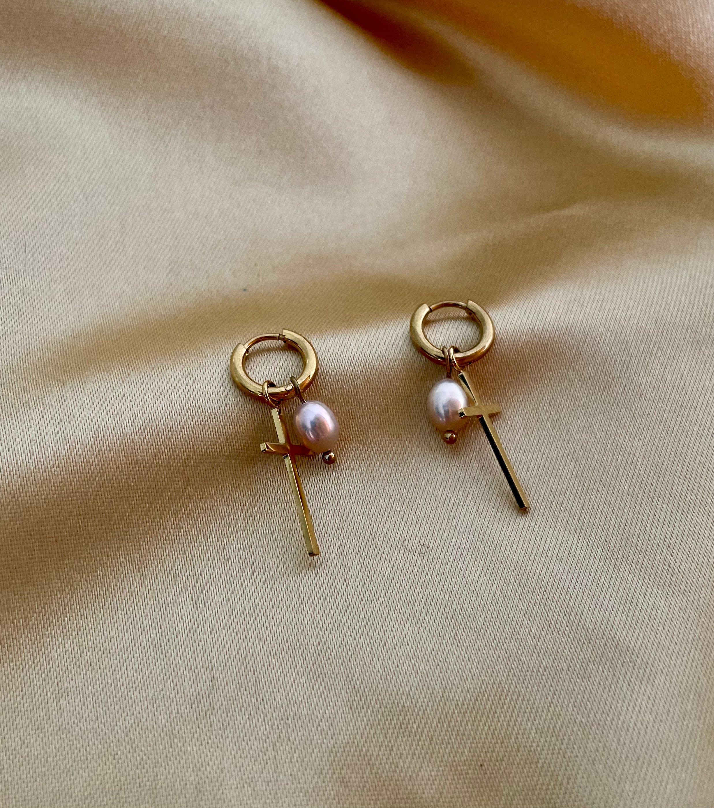 Pair of gold earrings with pearls on a beige fabric background