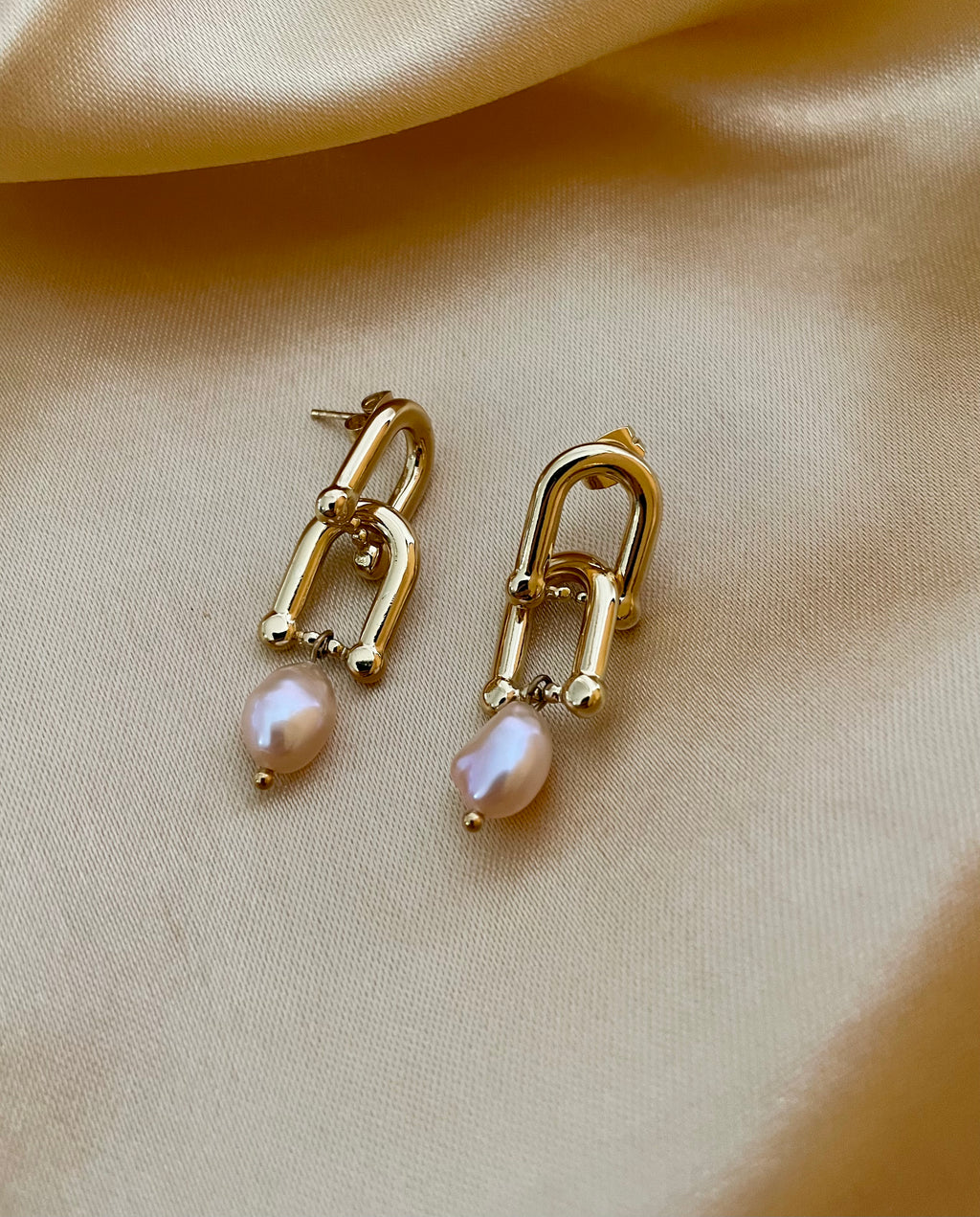 Pair of minimalist gold structural earrings with pink pearls, commercial jewelry photography on satin texture