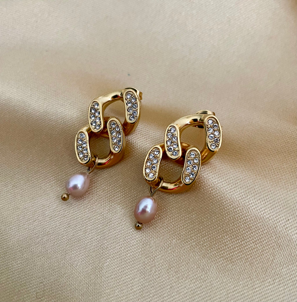 Gold chain earrings with pearl drops on a beige fabric background