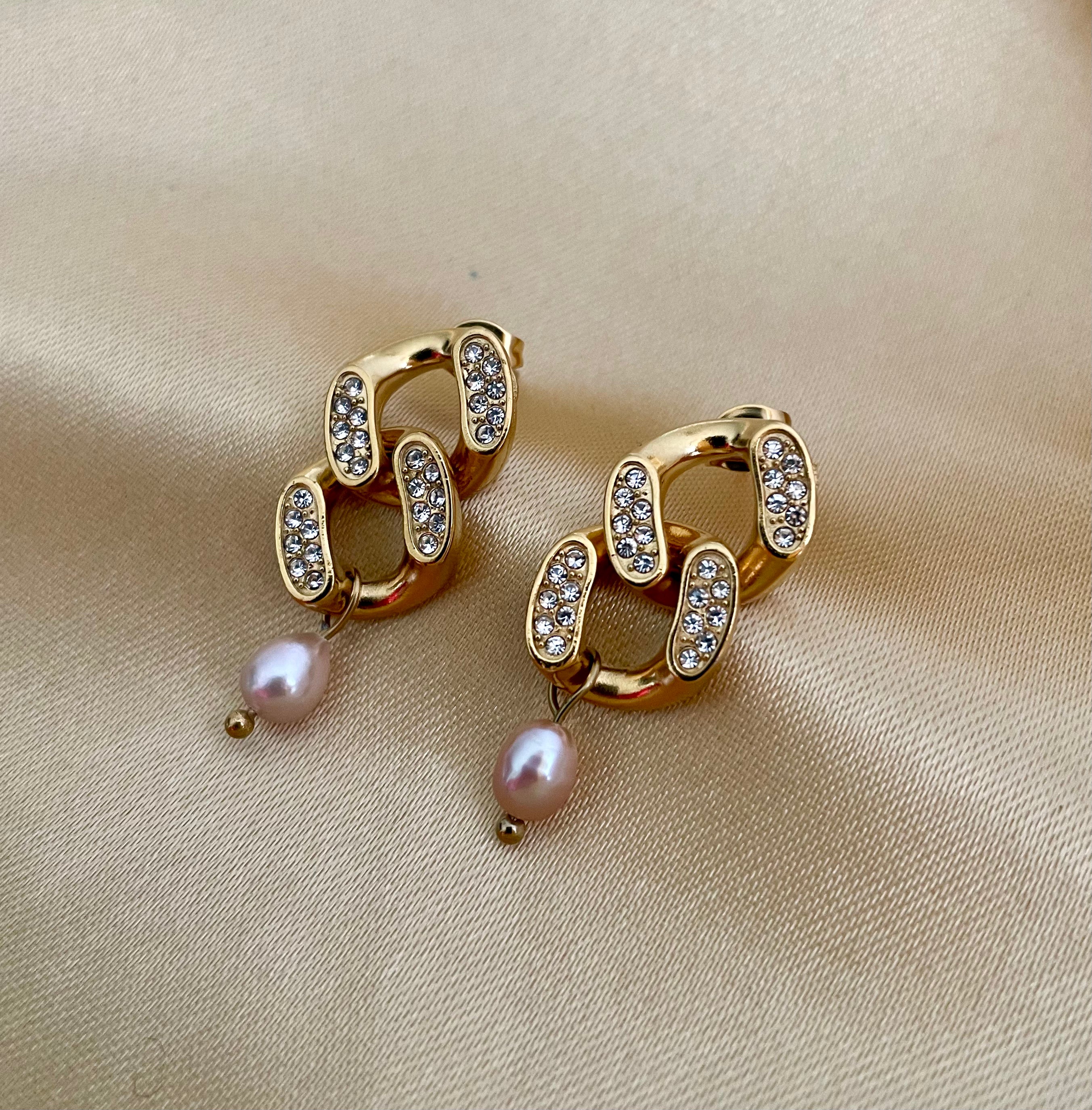 Gold chain earrings with pearl drops on a beige fabric background
