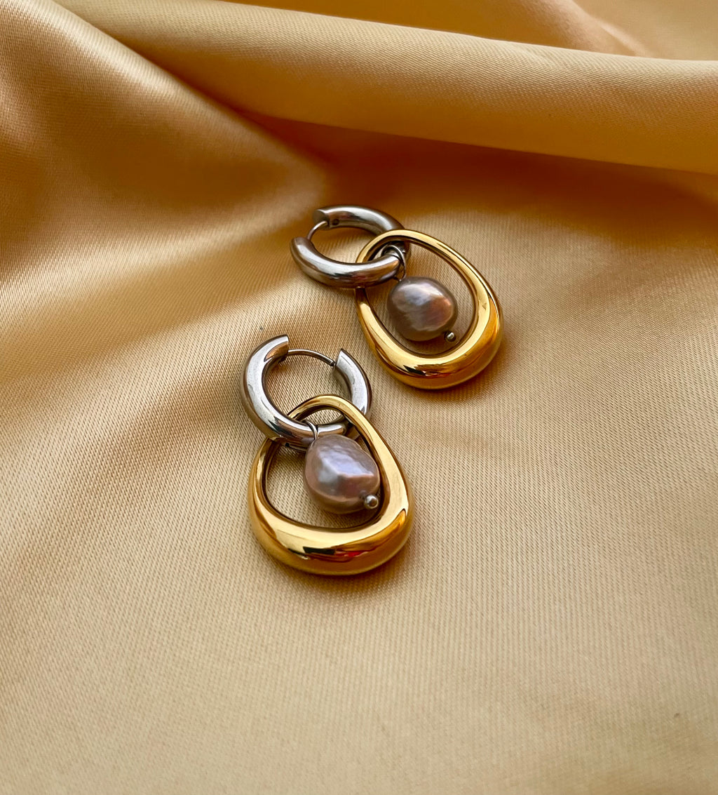 Gold and silver earring with a baroque round grey pearl drop worn by a person.