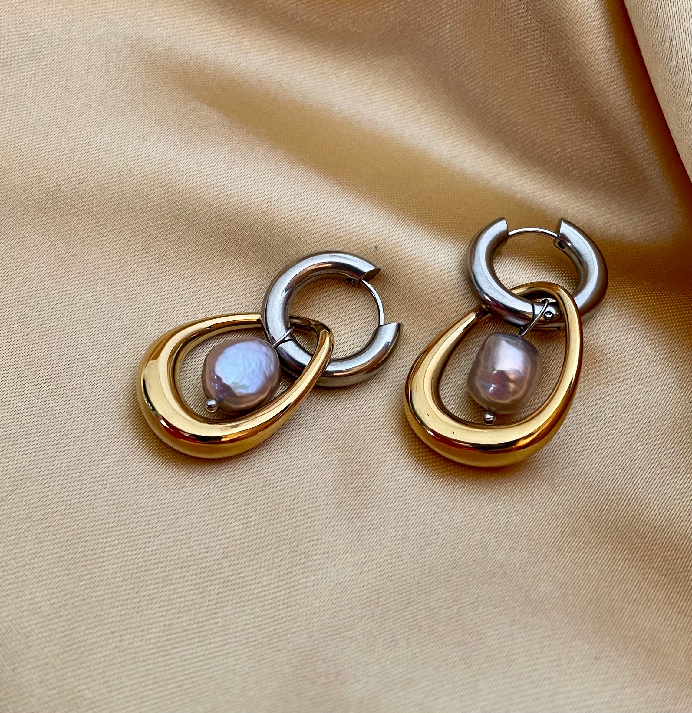 Gold and silver earring with a baroque round grey pearl drop worn by a person.