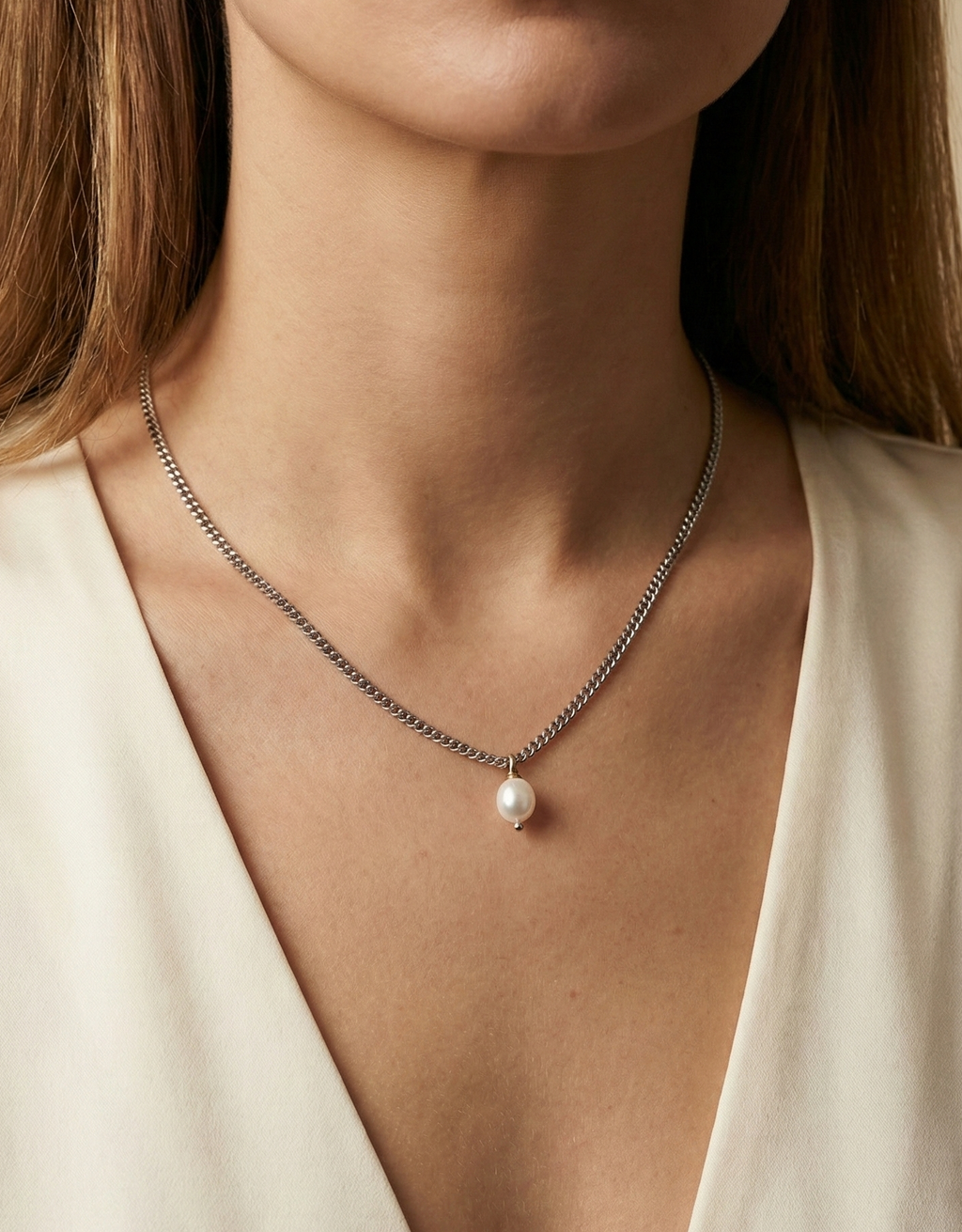 Silver necklace with a pearl pendant worn by a person