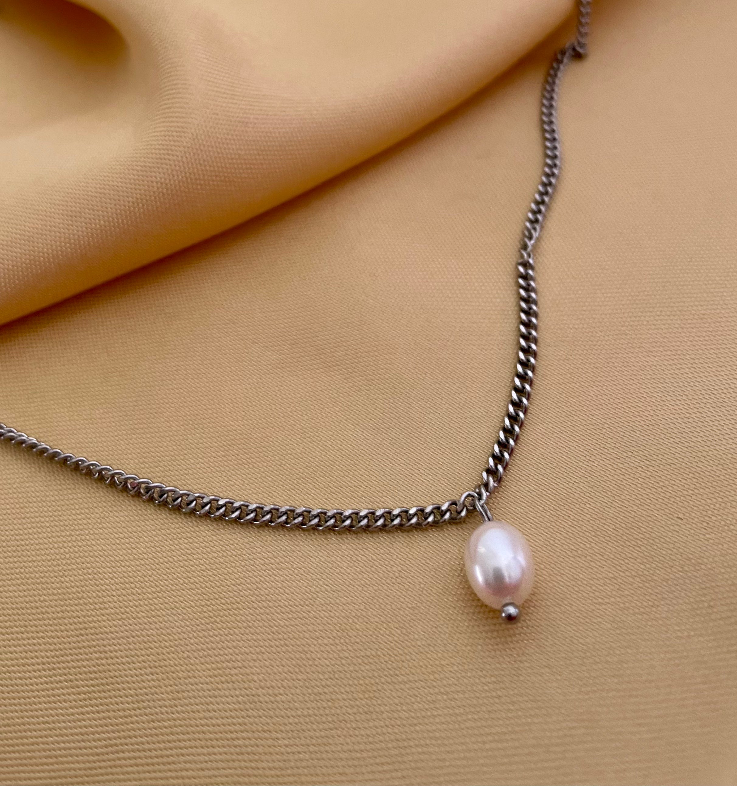 Necklace with a single pearl pendant on a beige fabric background