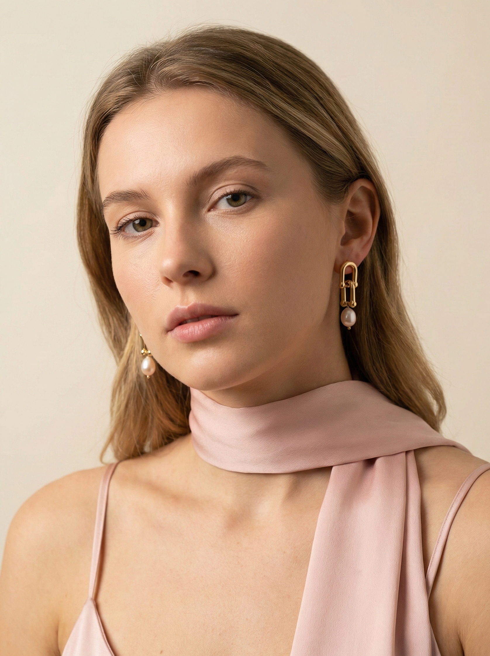Editorial portrait of a woman wearing gold link drop earrings with pink pearls, styled with a soft pink silk scarf