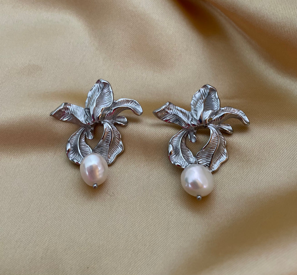 Macro detail showing the intricate textures of handcrafted silver flower earrings and the iridescence of the freshwater pearl attached