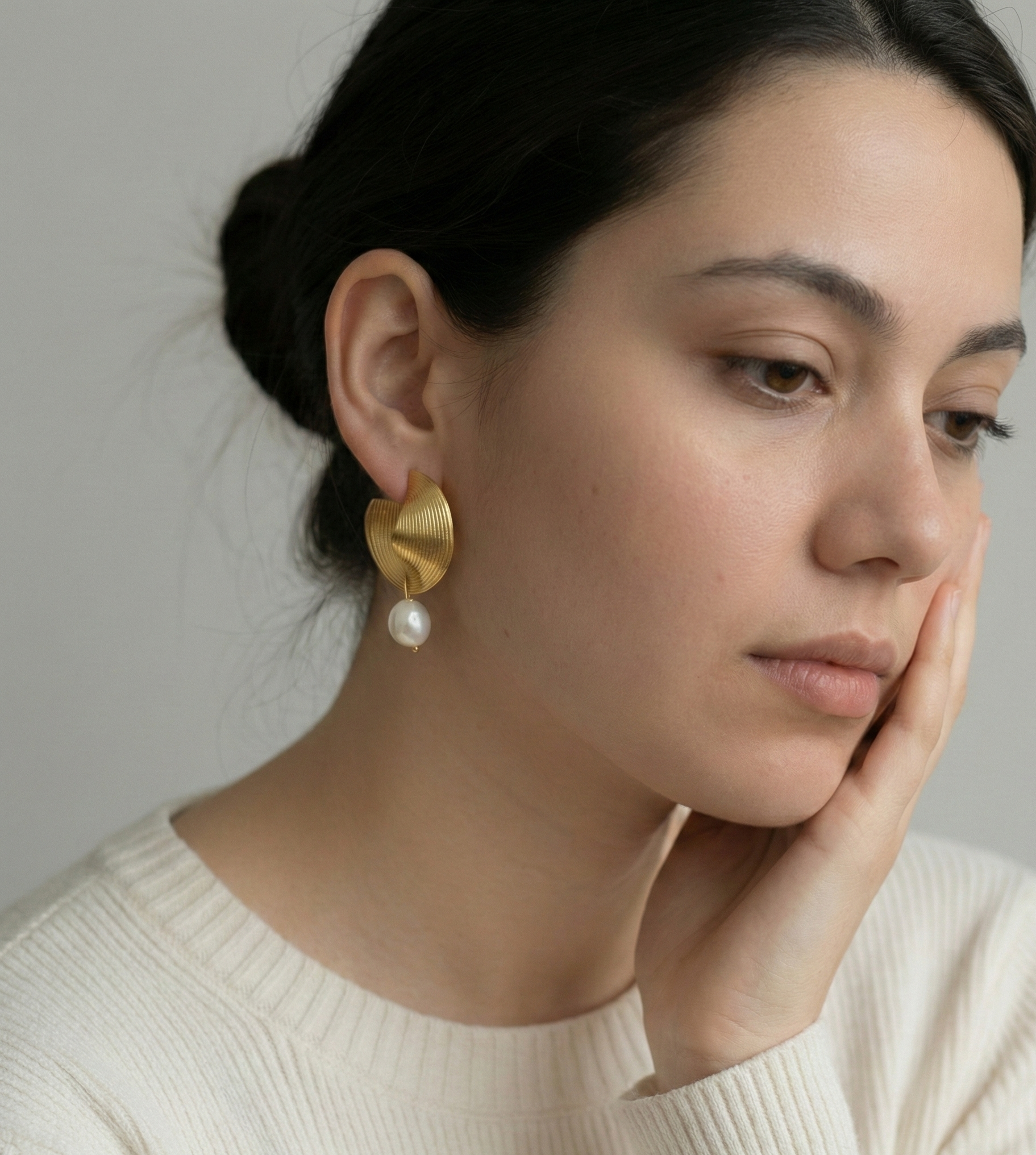 Close-up of ribbed yellow gold shell earrings featuring a round white pearl drop, worn by a model with beautiful hair.