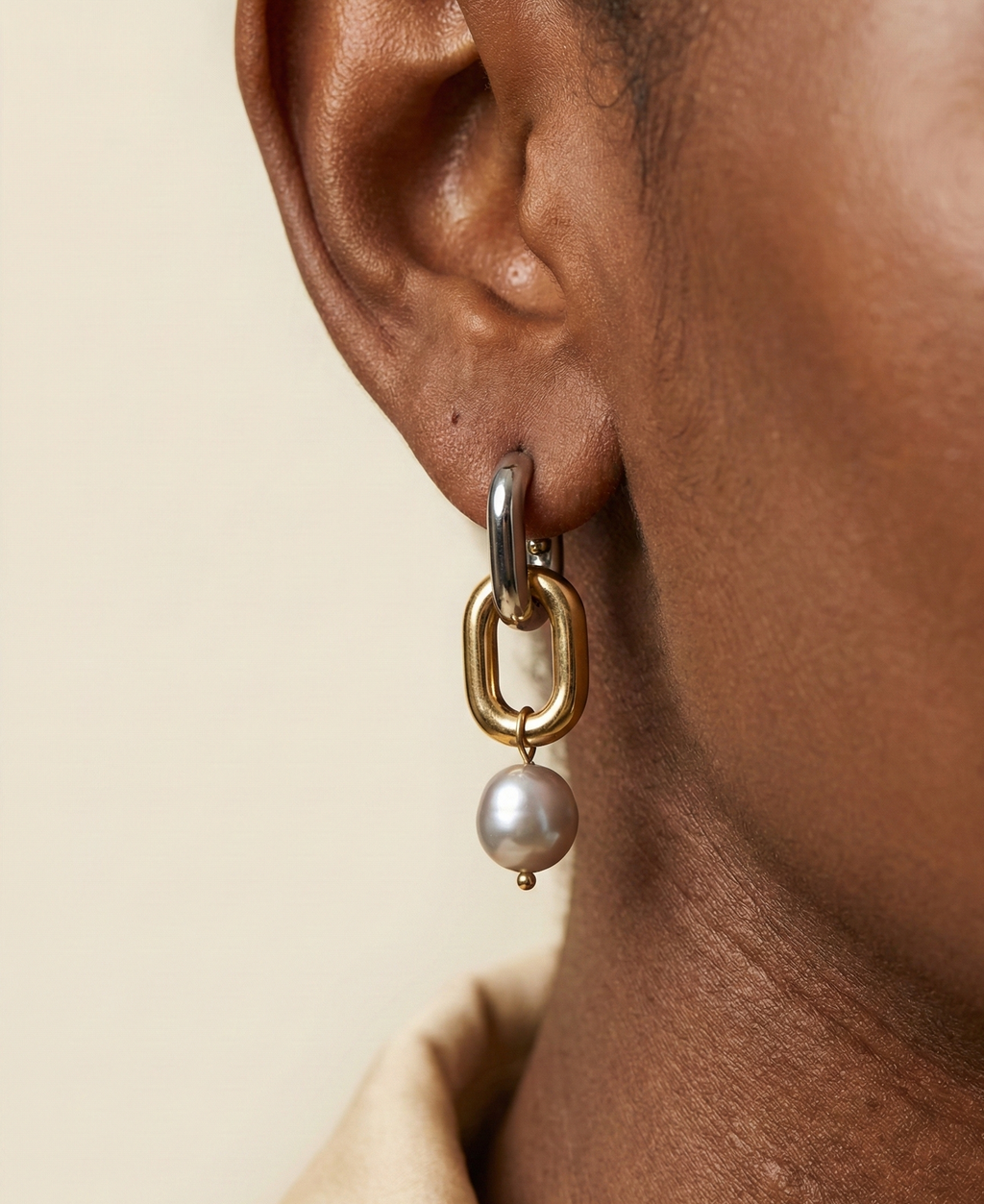 Close-up detail of mixed metal chain link earrings with grey pearl drops worn on the ear.
