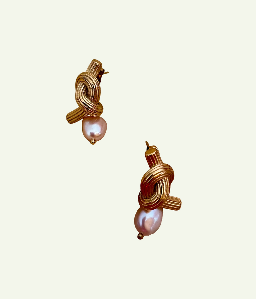 Close-up editorial photography of ribbed gold twisted knot earrings featuring a lustrous pink oval pearl drop